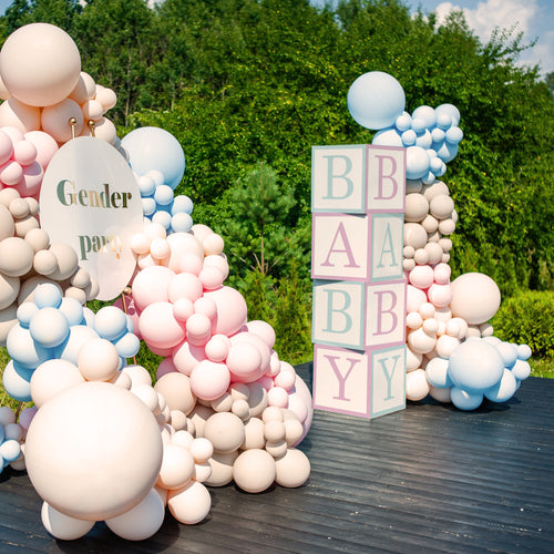 Decorative setup with balloons and baby blocks for a gender reveal party outdoors.